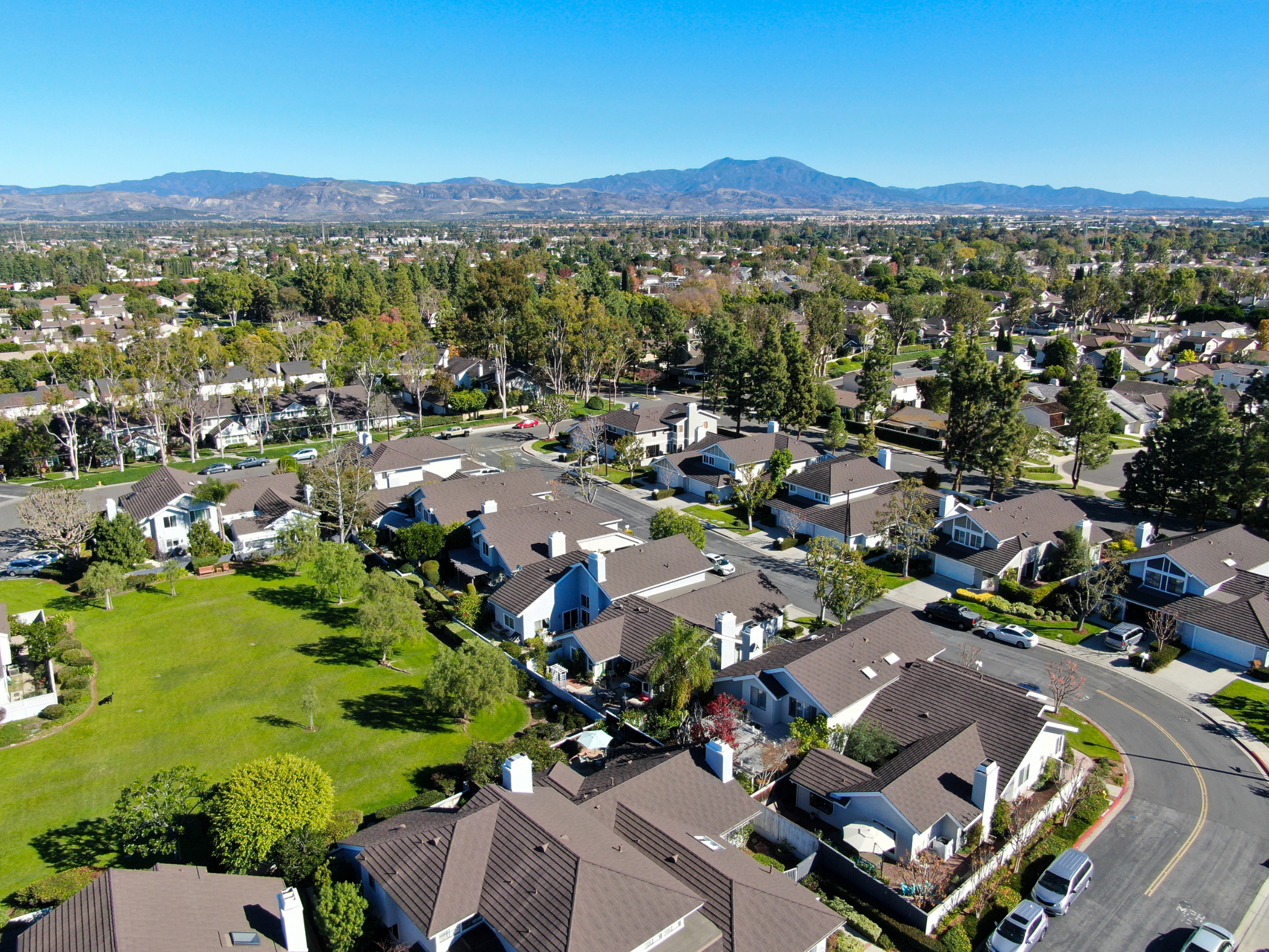 Row of modern townhomes with dark roofs, glass balcony railings, and clear blue sky.