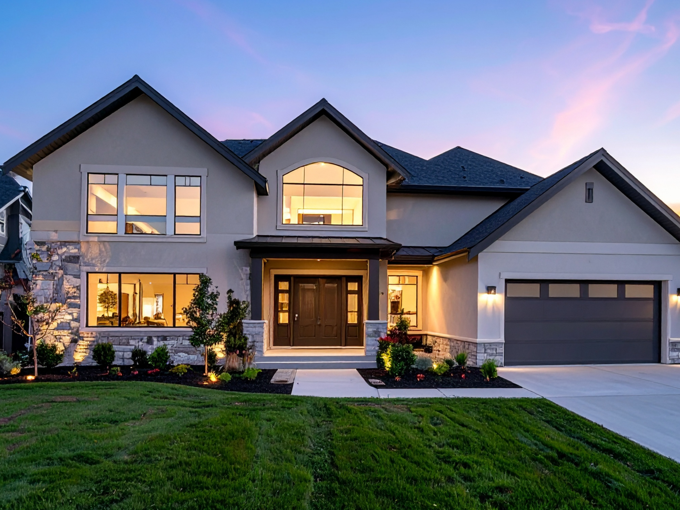 Two-story suburban home at twilight with stone accents, windows lit, and landscaped front yard.